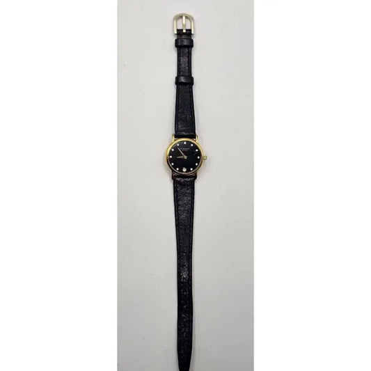 A vintage-style wristwatch with a black textured strap, a gold-tone case, and a black dial with simple hour markers, shown against a plain light gray background.