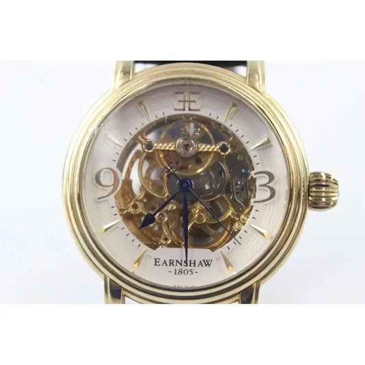 A gold-tone Earnshaw skeleton watch with a white dial and visible internal mechanical gears, shown against a plain white background.
