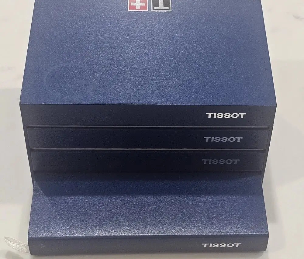 Three stacked Tissot watch boxes in a dark blue textured finish, with the Tissot logo printed on the front and top.