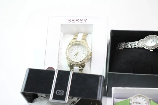 Two women's analog watches displayed in their boxes on a white background. One watch is gold with a white dial and crystal-embellished bezel, shown in a white SEKSY box.