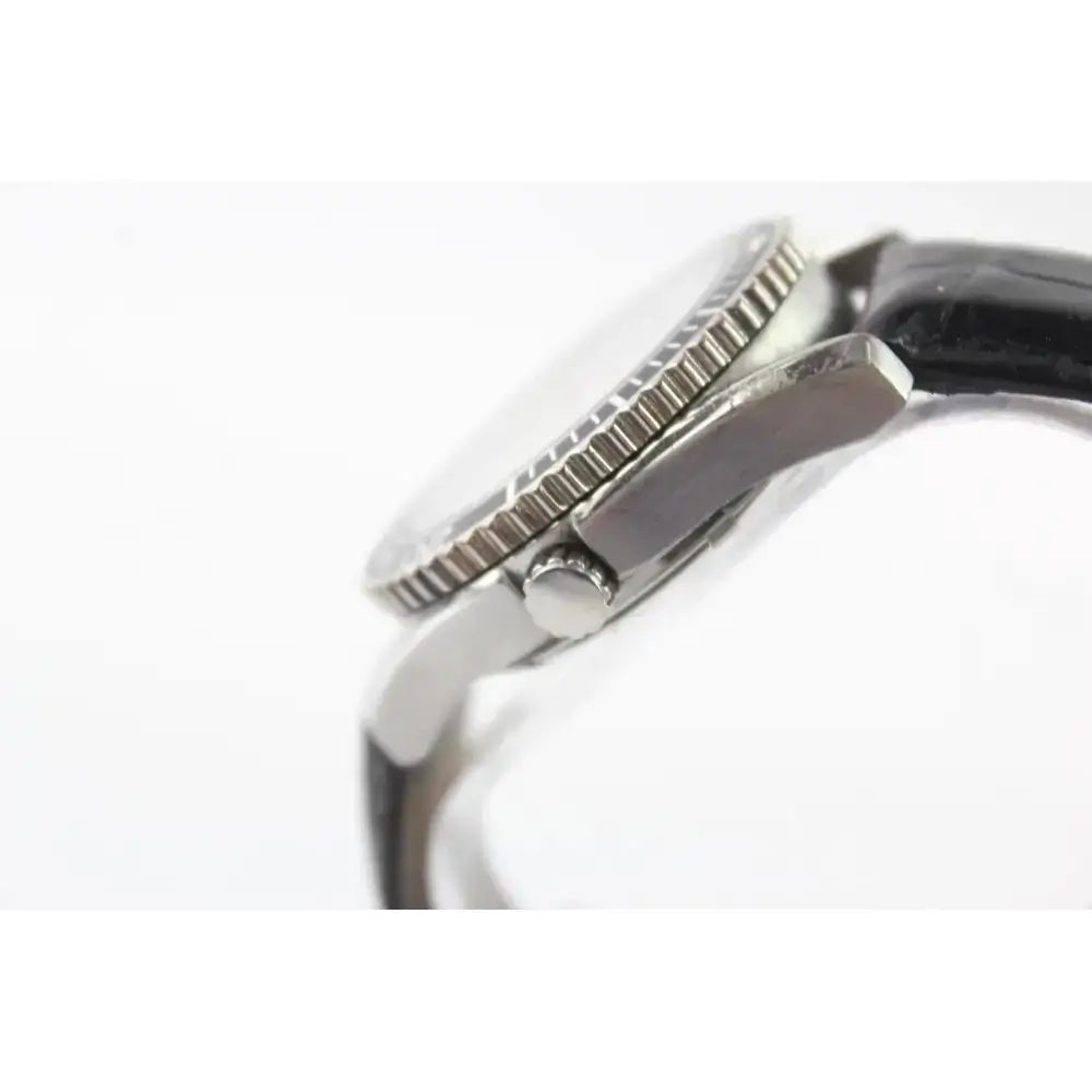 Close-up side view of a wristwatch showing a silver-toned metal case with a textured bezel and a dark strap on a white background.