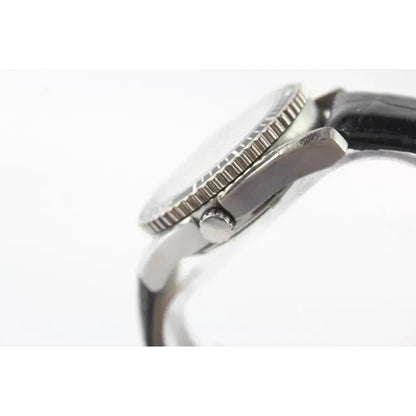 Close-up side view of a wristwatch showing a silver-toned metal case with a textured bezel and a dark strap on a white background.