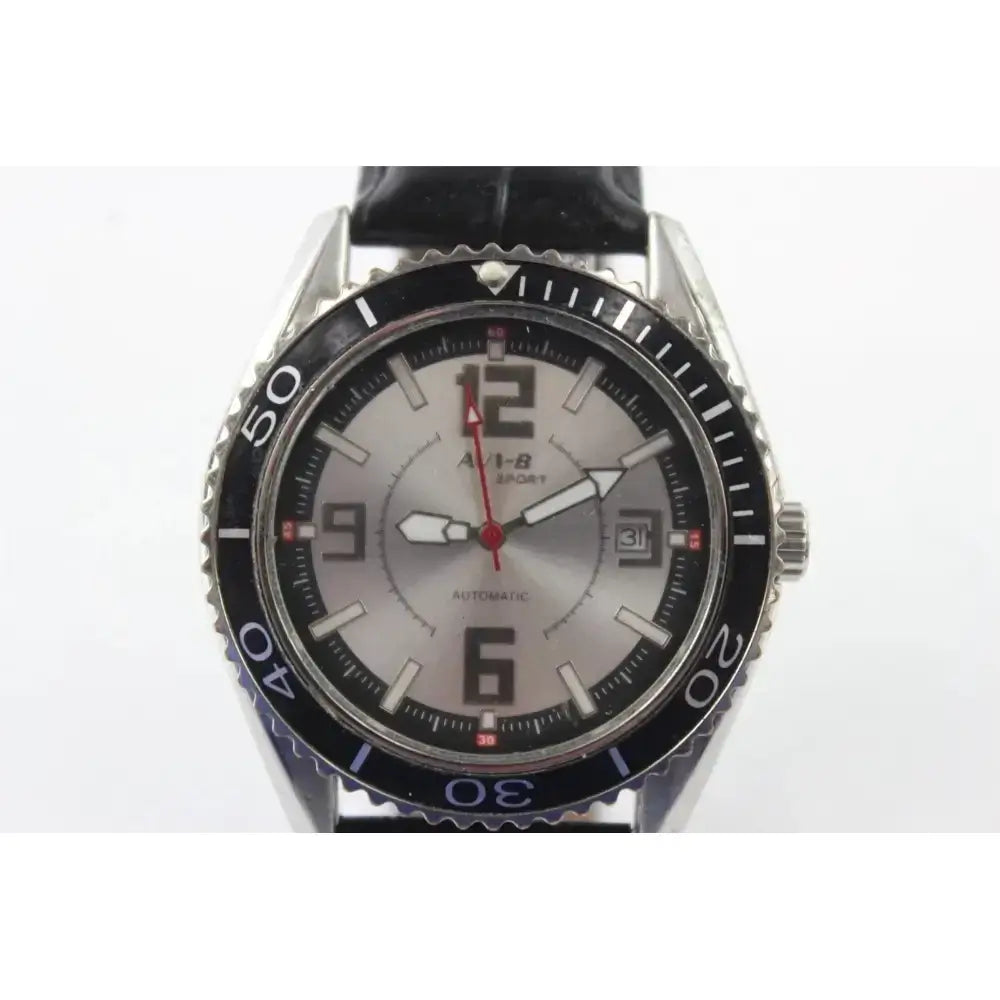 A wristwatch with a silver-toned stainless steel case, a black rotating bezel, and a silver dial featuring large black Arabic numerals and a red second hand. The watch is fitted with a black leather strap and has 'AUS-B' branding printed on the dial.