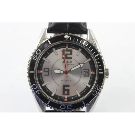 A wristwatch with a silver-toned stainless steel case, a black rotating bezel, and a silver dial featuring large black Arabic numerals and a red second hand. The watch is fitted with a black leather strap and has 'AUS-B' branding printed on the dial.