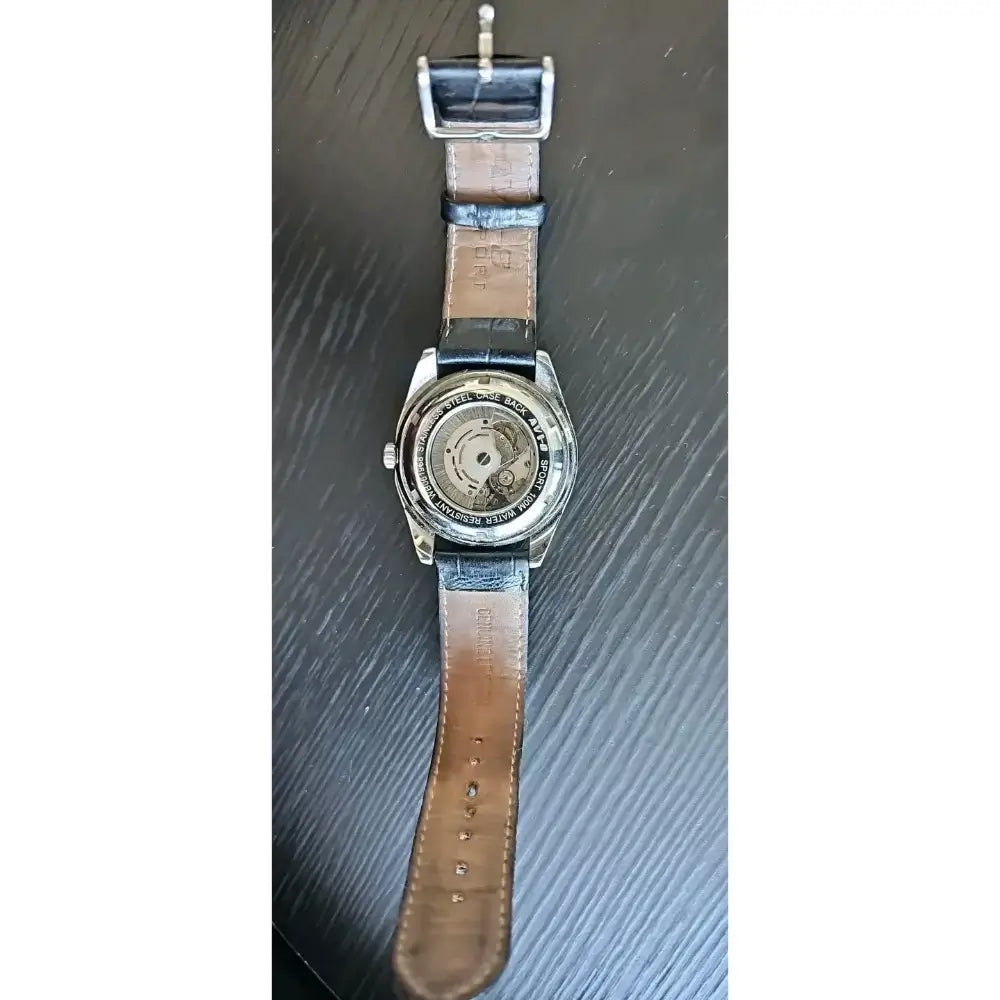 A vintage wristwatch with a brown leather strap and a silver-toned case showing a transparent dial, displayed vertically on a dark wood-grained surface.