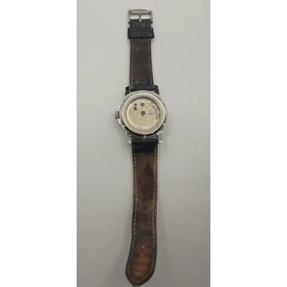 A vintage wristwatch with a brown leather strap and a silver-toned case, shown with the back cover open to reveal the mechanical movement inside, set against a plain light gray background.