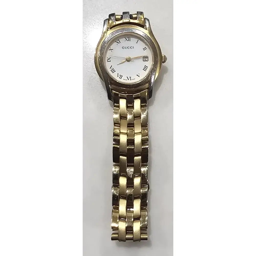 A Gucci women's analog watch with a gold-tone metal link bracelet, a silver-tone case, and a white dial with black Roman numerals and a date window.