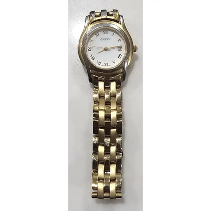 A Gucci women's analog watch with a gold-tone metal link bracelet, a silver-tone case, and a white dial with black Roman numerals and a date window.