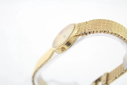 A close-up shot of a gold-tone mesh bracelet watch with a round dial, shown against a plain white background.
