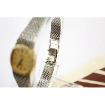 A vintage women's watch with a silver-tone mesh bracelet and a gold-tone round dial, shown close-up with the clasp engraved with 'SWISS MADE'.
