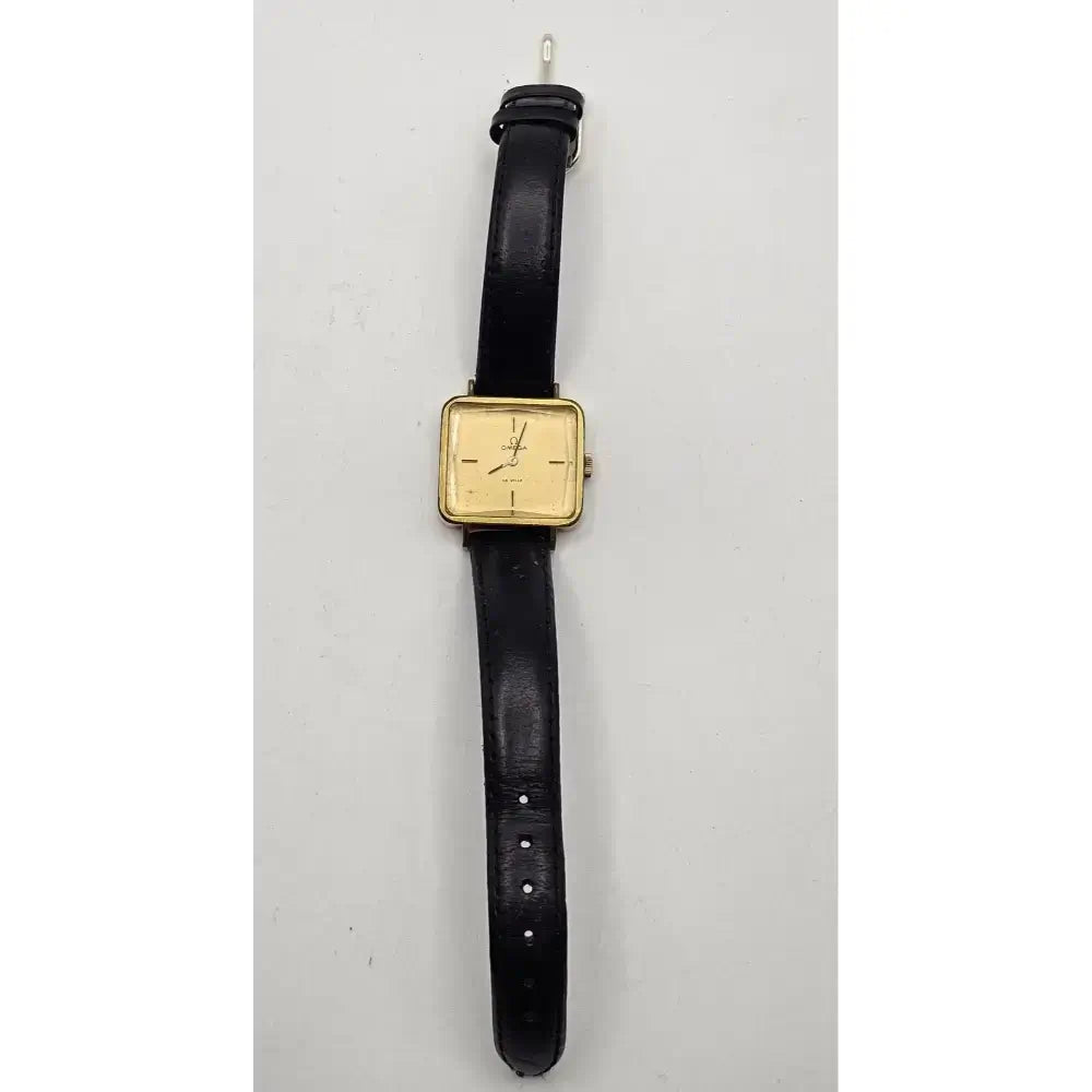 A vintage wristwatch with a square gold-tone dial and a black leather strap, shown against a plain light gray background.