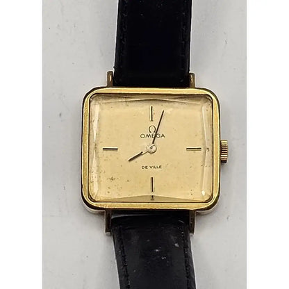 Omega De Ville vintage wristwatch with a gold-tone square case, cream-colored dial, and black leather strap, shown against a light gray background.