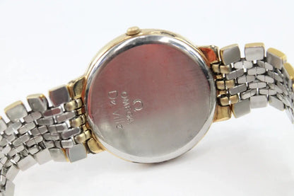 Close-up of the back of a two-tone metal wristwatch with a round silver case and matching metal bracelet, showing engraved 'OMEGA De Ville' text on the case.