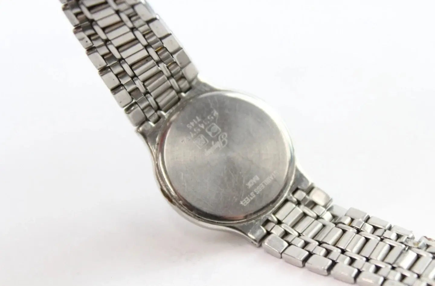 Close-up of the back of a silver metal wristwatch with a link bracelet on a plain white background.