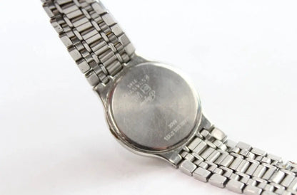 Close-up of the back of a silver metal wristwatch with a link bracelet on a plain white background.