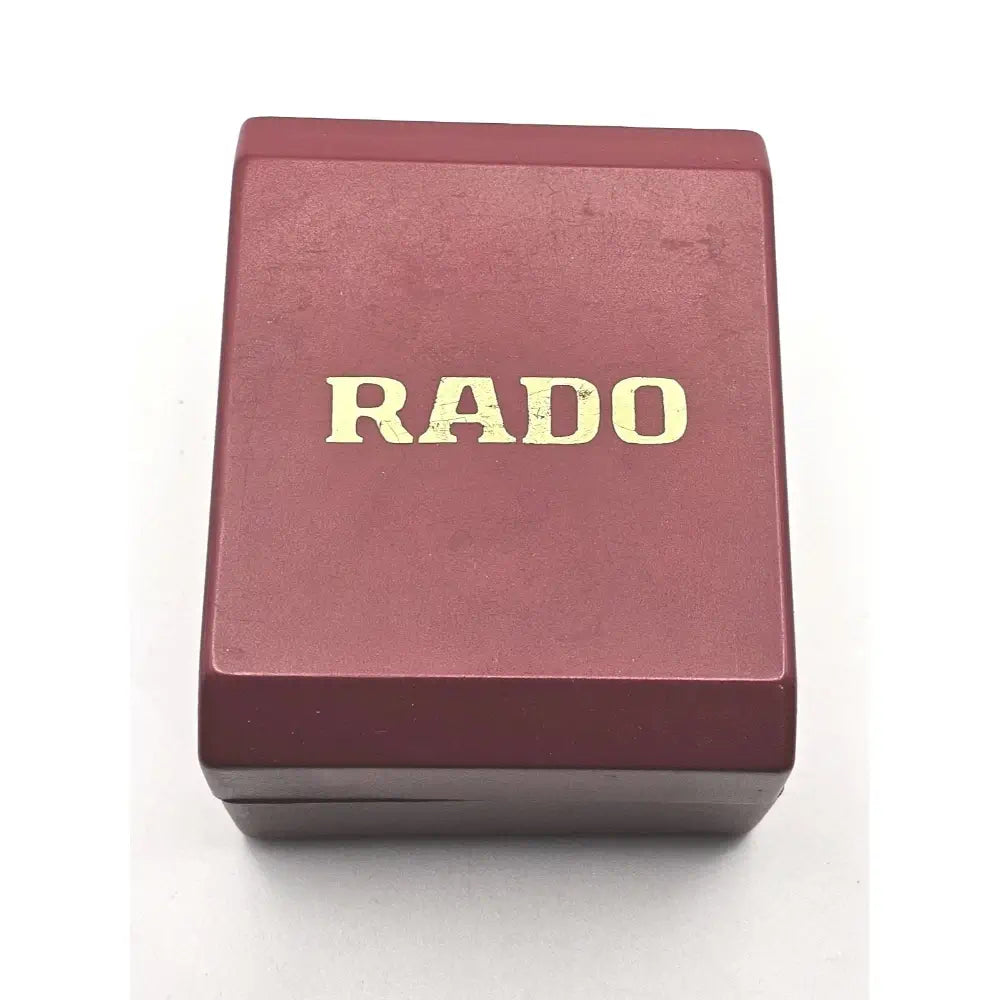 A rectangular dark red RADO watch box with gold lettering on a white background.