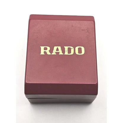 A rectangular dark red RADO watch box with gold lettering on a white background.