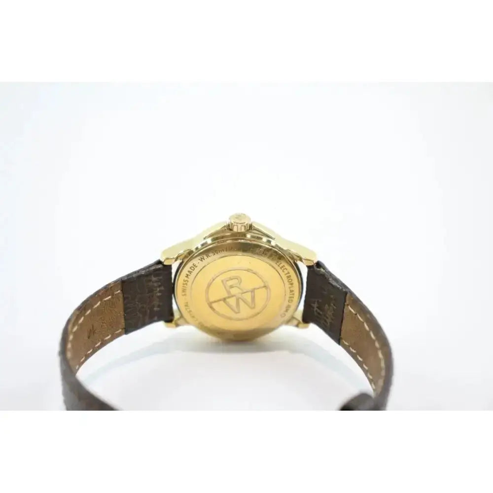 A vintage wristwatch shown from the back, featuring a gold-toned case with an engraved logo and a dark brown leather strap.