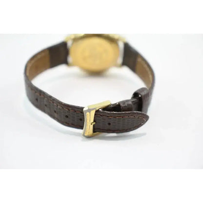 A close-up of a watch strap with a textured dark brown leather finish and a gold-tone buckle, shown from the back against a plain white background.
