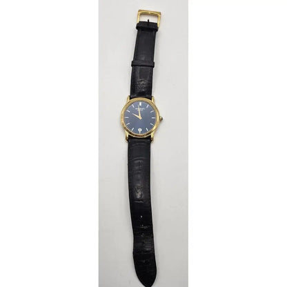 A vintage wristwatch with a round gold-tone case, a blue dial, and a black leather strap, shown vertically against a light gray background.