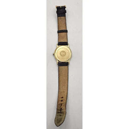 A vintage wristwatch shown from the back, featuring a gold-toned case and a distressed tan leather strap with black stitching and black loops.