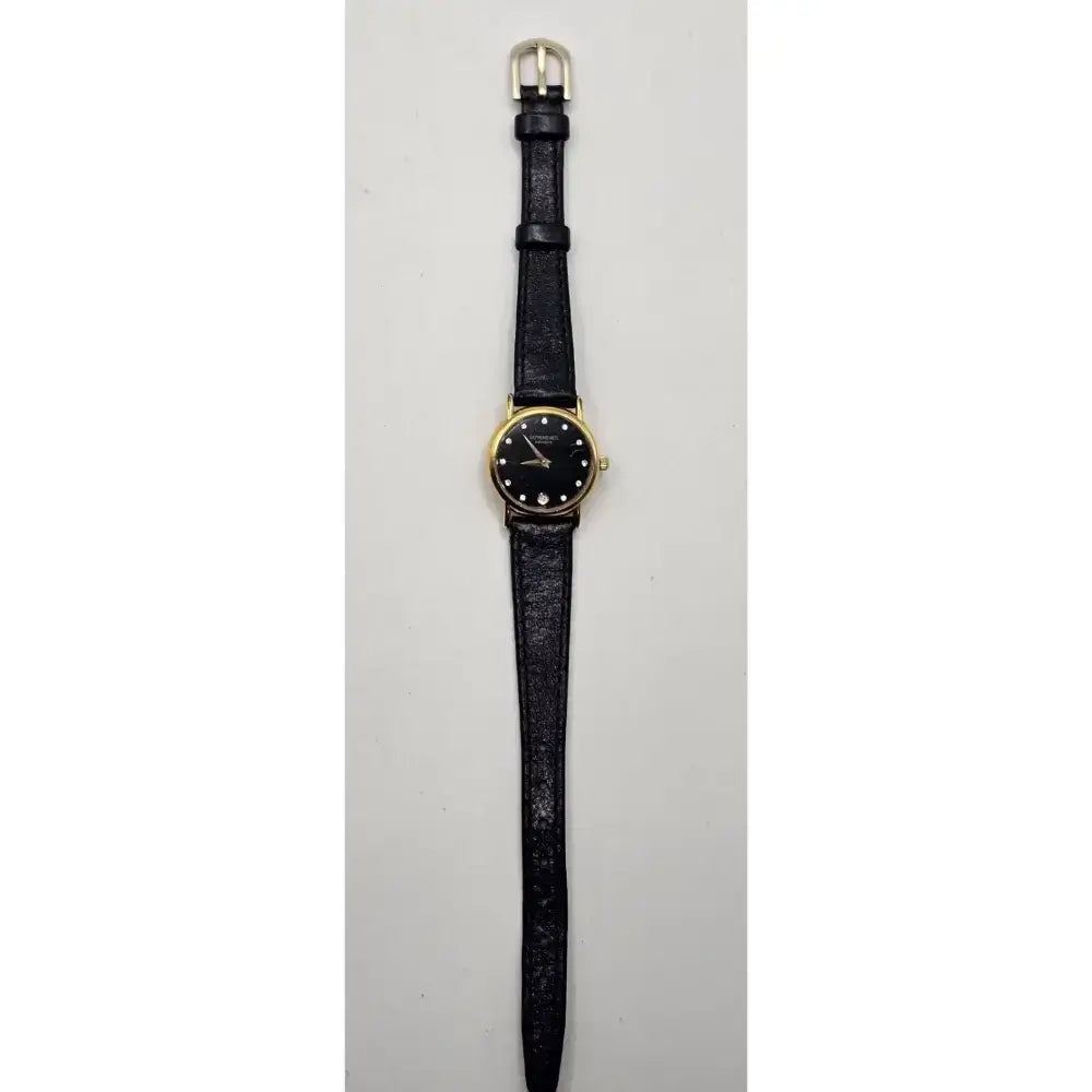 A vintage-style wristwatch with a black textured strap, a gold-tone case, and a black dial with simple hour markers, shown against a plain light gray background.