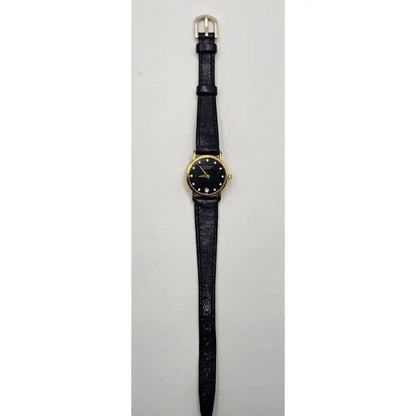 A vintage-style wristwatch with a black textured strap, a gold-tone case, and a black dial with simple hour markers, shown against a plain light gray background.