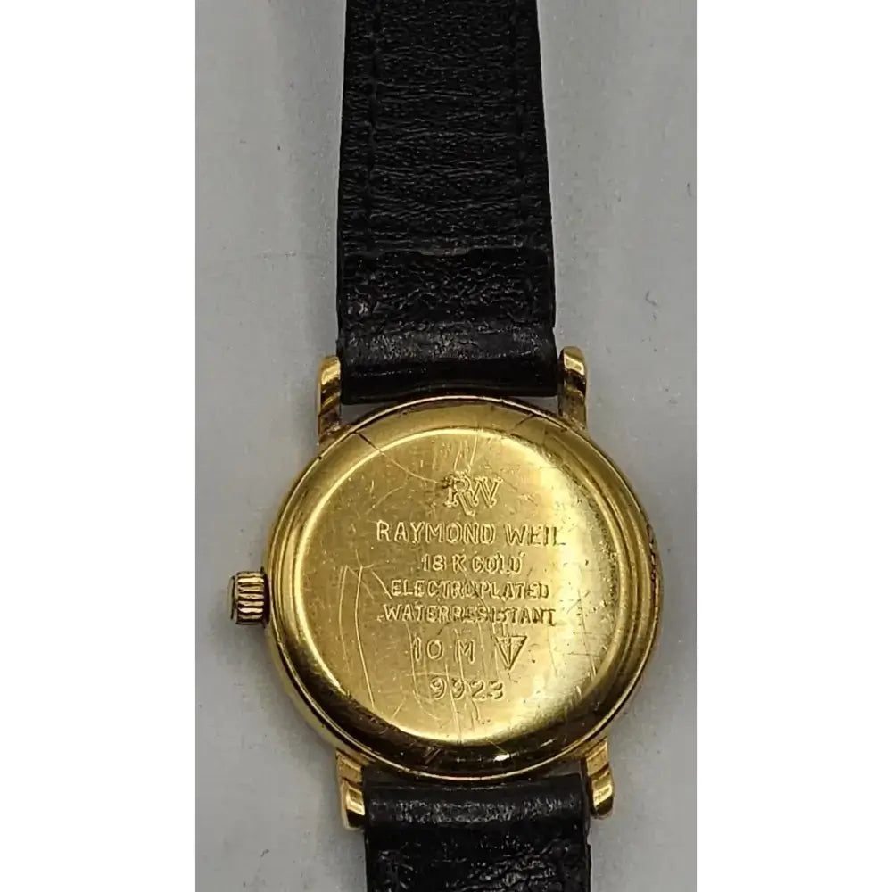 Back view of a vintage Raymond Weil wristwatch with a gold-toned case and a black leather strap, showing engraved details on the case.