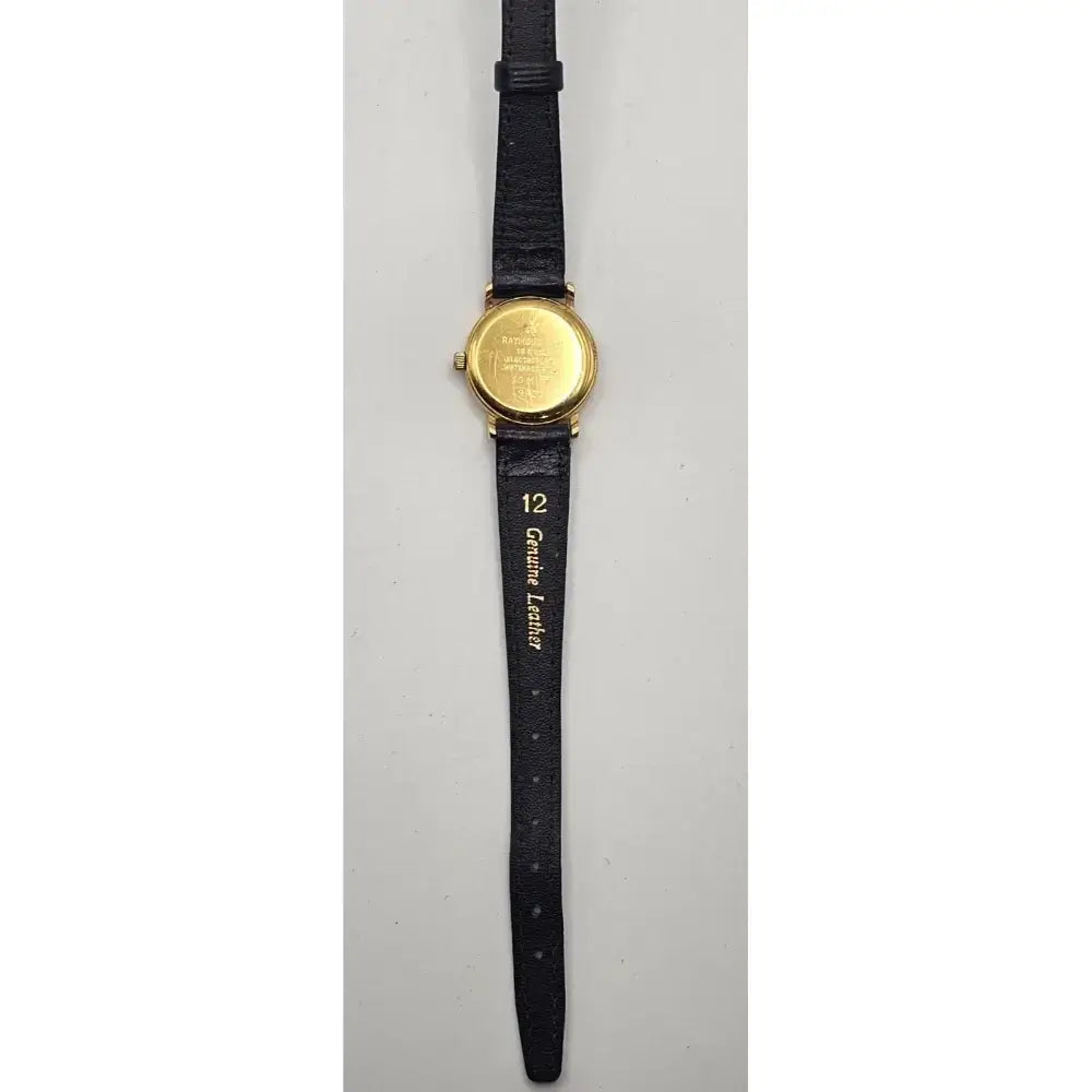 A vintage wrist watch with a round gold-tone case and a black leather strap, shown from the back against a light gray background.