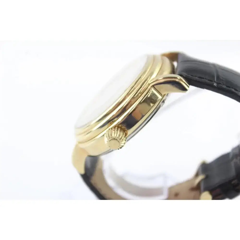 Close-up side view of a gold-tone wristwatch with a black leather strap on a white background.