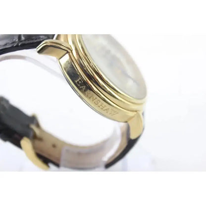 Close-up of a wristwatch showing a gold-toned case with the brand name 'FAUXHANI' engraved on the side, paired with a black leather strap on a white background.