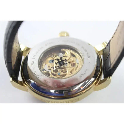 Close-up of the back of a wristwatch with a gold-tone case, transparent crystal cover, visible mechanical movement, and a dark leather strap on a white background.