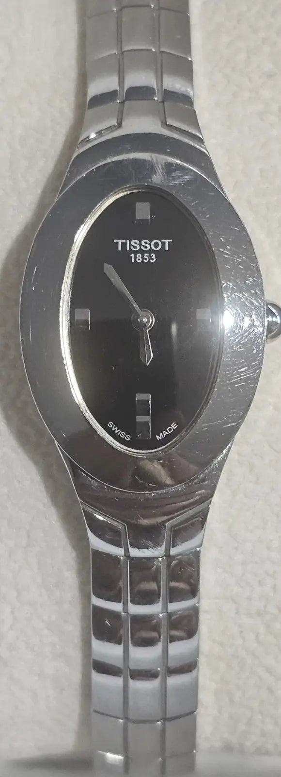 A Tissot 1853 women's analog watch with a silver-tone stainless steel case and bracelet, featuring a black dial with silver-tone hands and hour markers.