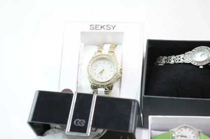 Two women's analog watches displayed in their boxes on a white background. One watch is gold with a white dial and crystal-embellished bezel, shown in a white SEKSY box.