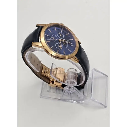 A men's luxury watch with a blue dial, gold-tone case, and black leather strap, displayed on a clear plastic stand against a light gray background.