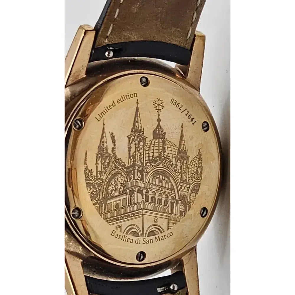 Close-up of the back of a vintage watch with a gold-toned case and a brown leather strap. The round case is engraved with a detailed illustration of the Basilica di San Marco in Venice, along with the text 'Limited edition' and '0582 / 1981'.