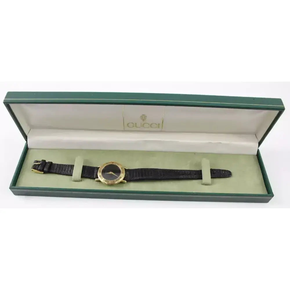 A Gucci wristwatch with a black leather strap and gold-tone case, presented inside its original green and beige Gucci box.