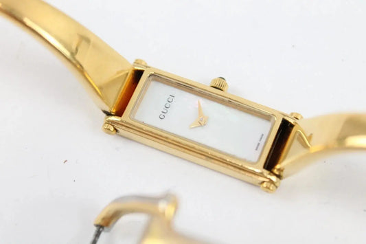 A Gucci gold-tone metal watch with a rectangular white dial and a matching gold-tone bracelet, shown on a plain white background.