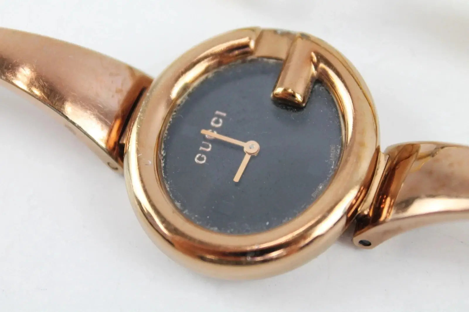 A close-up of a Gucci wristwatch with a rose gold-tone metal bracelet and case, featuring a dark blue dial with gold-tone hands and the Gucci logo.