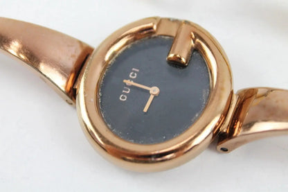 A close-up of a Gucci wristwatch with a rose gold-tone metal bracelet and case, featuring a dark blue dial with gold-tone hands and the Gucci logo.