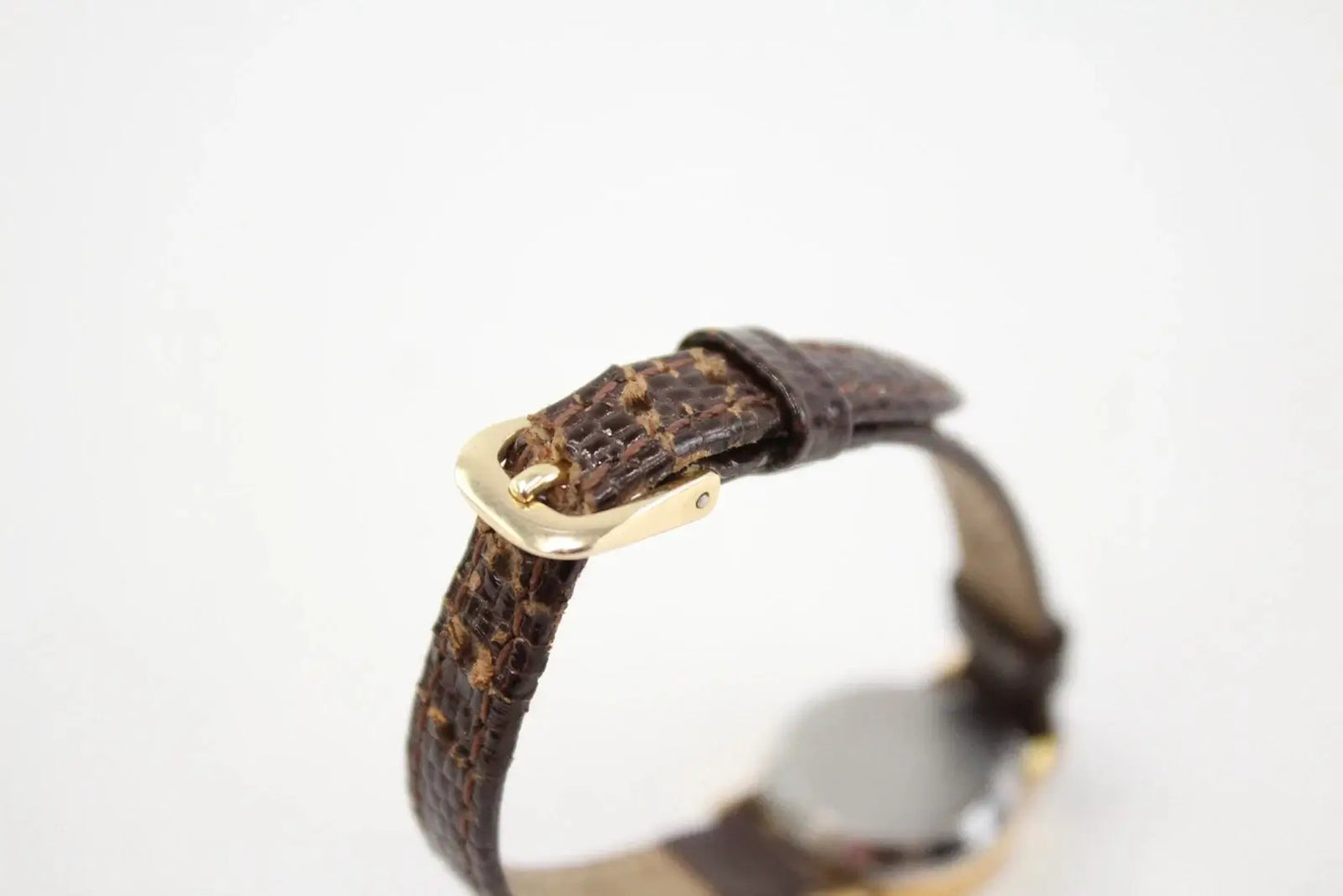 A close-up of a dark brown textured leather watch strap with a gold-tone buckle, shown against a plain white background.