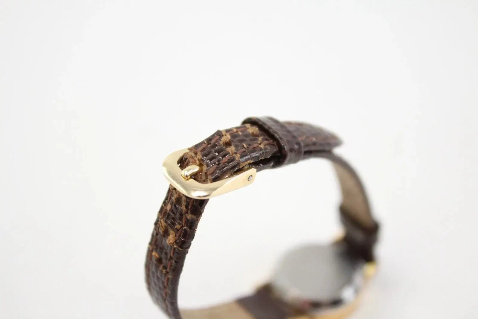 A close-up of a dark brown textured leather watch strap with a gold-tone buckle, shown against a plain white background.
