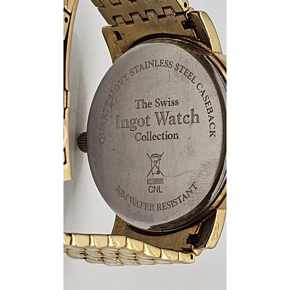 Close-up of the back of a wristwatch showing a brushed stainless steel caseback engraved with 'The Swiss Ingot Watch Collection' and 'Quartz-Move Stainless Steel Caseback', with a gold-tone metal bracelet visible around it.