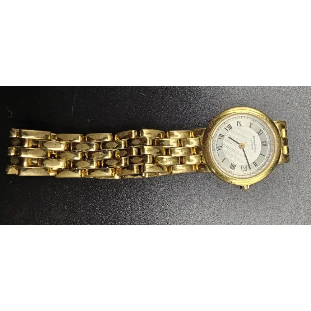 A vintage-style gold-tone wristwatch with a matching gold-tone link bracelet, featuring a white dial with black Roman numerals and hands, photographed against a dark textured background.