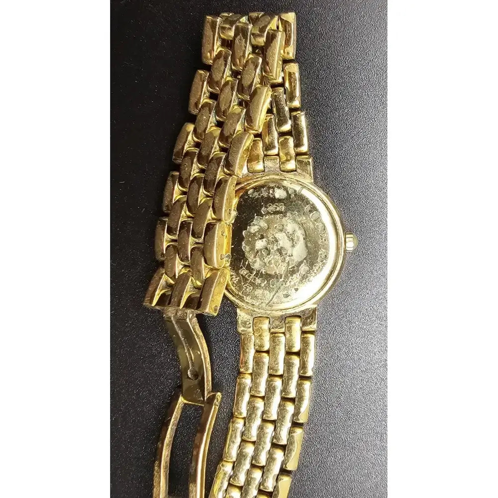 A vintage gold-tone metal link watch with a round case, shown on a dark textured background.