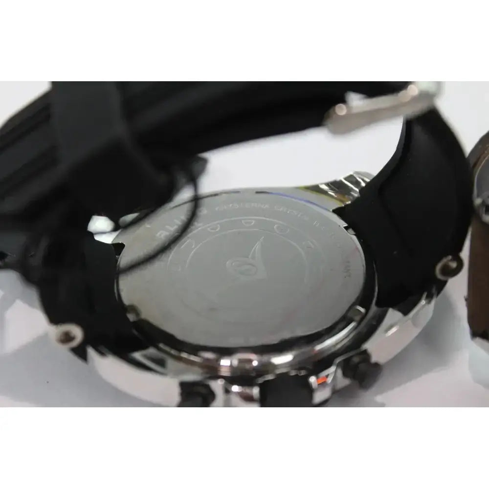 Close-up of the back of a wristwatch with a black strap, silver-tone case, and a brushed metal case back featuring a logo and text.