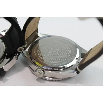 Close-up of the back of a wristwatch with a silver metal case and a dark strap, showing engraved branding and details on the case lid.