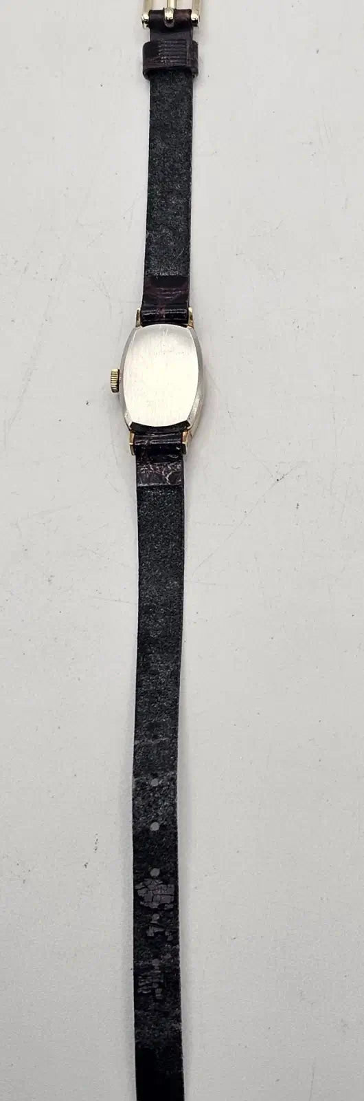 A vintage oval watch with a black leather strap and a silver-toned case featuring a white dial, shown against a plain light gray background.