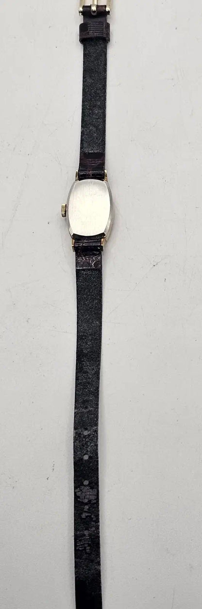 A vintage oval watch with a black leather strap and a silver-toned case featuring a white dial, shown against a plain light gray background.