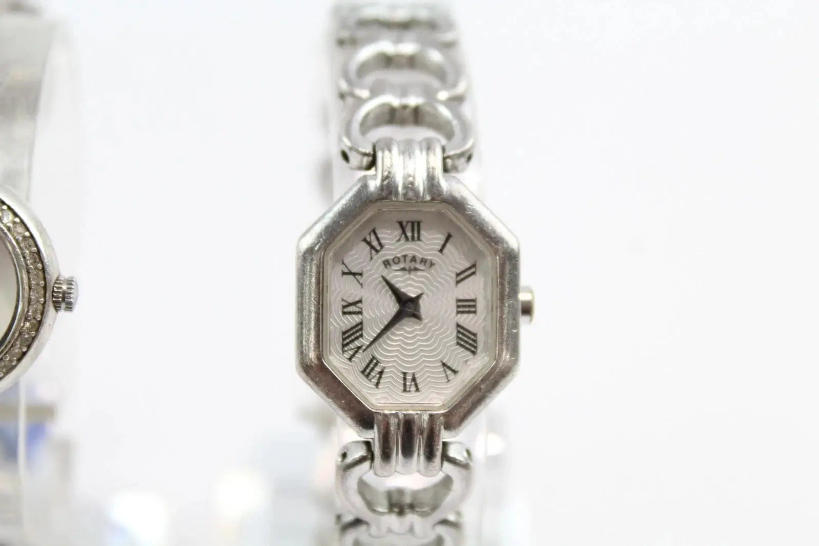 A silver-tone octagonal analog watch with a white dial, black Roman numerals, and a matching silver link bracelet, shown against a white background.